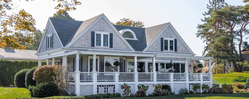 Classic New England cape house with wrap-around porch and green lawn